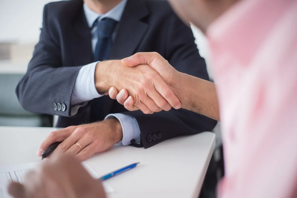 Two people shaking hands across a table, the in-person deal a local cash home buyer offers versus an iBuyer