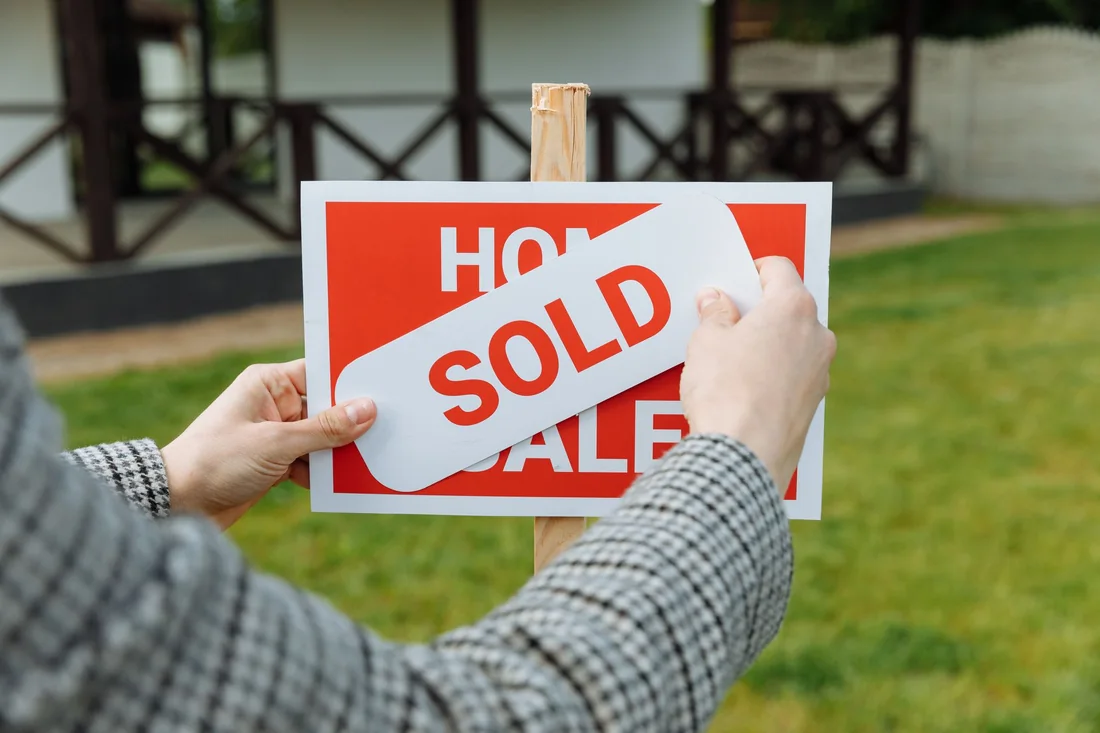 A realtor posting a sold sticker on a for-sale sign after a house sale in Iowa