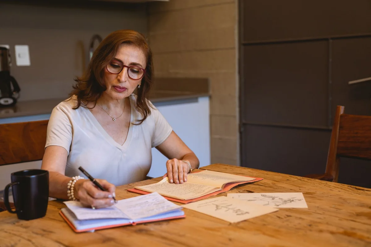 A person writing notes at a kitchen table, working through the checklist for selling as-is versus fixing up