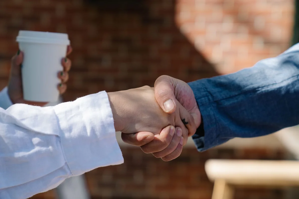 Two people shaking hands in front of a house, a cash buyer taking a home with an open insurance claim as-is