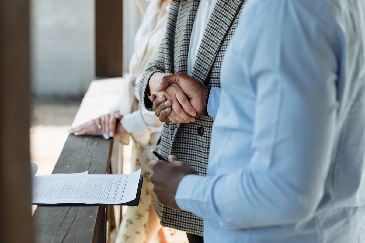 A home seller and a buyer shaking hands, closing a cash sale on an Iowa house with no central air