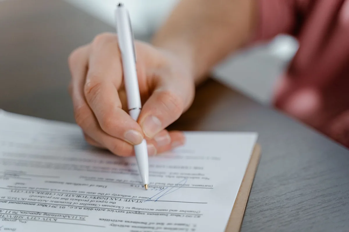 A hand signing a deed document with a pen, showing how a quitclaim deed transfers interest